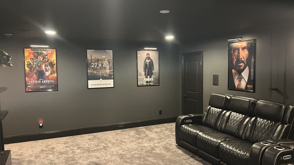 Framed movie posters hung evenly with individual picture lights along a home theater wall, Nashville TN