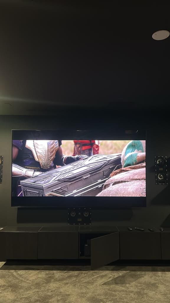 Close view of a mounted home theater TV with the center channel below and surround speakers on each side, Nashville TN