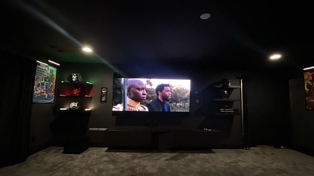 Wall mounted TV flanked by surround speakers in a darkened home theater room, Nashville TN