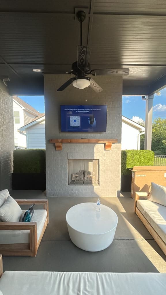 Outdoor TV mounted above a painted brick fireplace on a covered patio with ceiling fan, Nashville TN